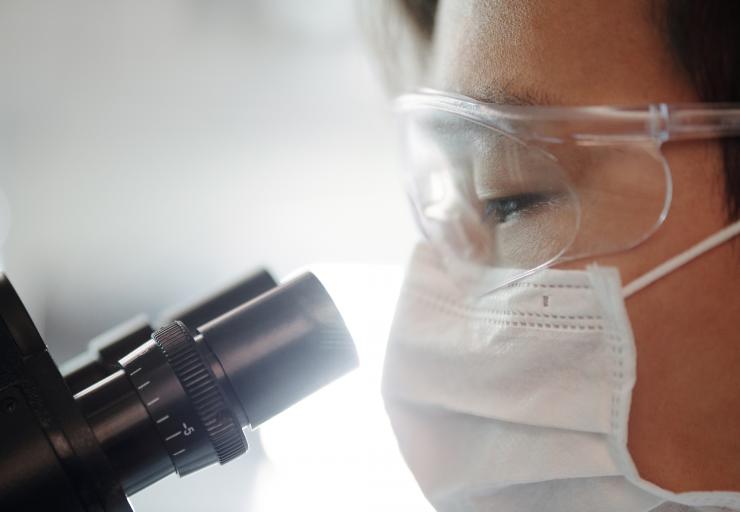 Masked person looking into microscope