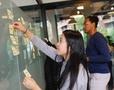 An Asian woman and Black man putting task post-it notes on a board